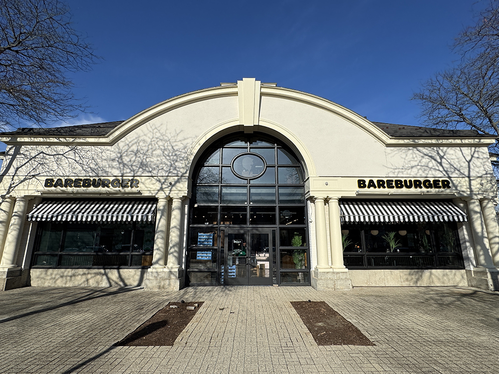 Exterior of Bareburger restaurant in Glastonbury, Connecticut, featuring a large arched entrance with black-and-white striped awnings, modern glass doors, and bold signage — serving organic grass-fed beef burgers, plant-based options, and family-friendly dining