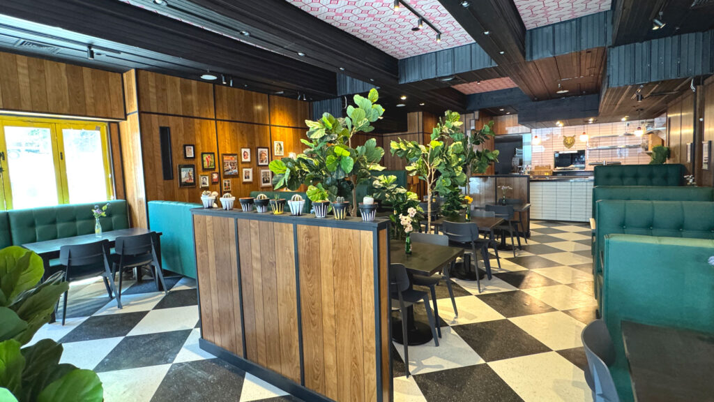 Interior of Bareburger’s Upper East Side restaurant in Manhattan, New York City, featuring retro wood paneling, green booth seating, black-and-white checkered floors, and modern dining tables — a cozy space to enjoy organic grass-fed burgers, plant-based options, and family-friendly meals