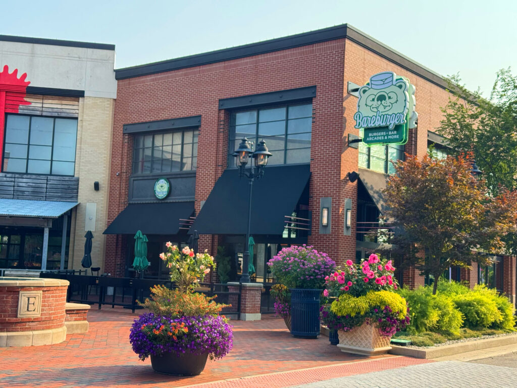 Exterior of Bareburger restaurant at Easton Gateway in Columbus, Ohio, featuring brick architecture, black awnings, colorful flower planters, and outdoor seating — serving organic grass-fed beef burgers, plant-based options, and family-friendly dining.